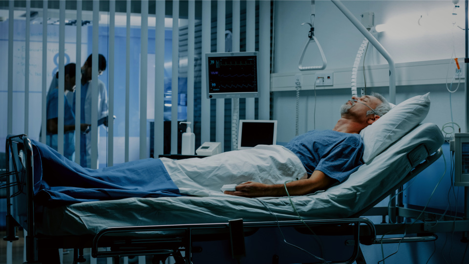 patient lying in hospital bed, with doctors having discussion outside room
