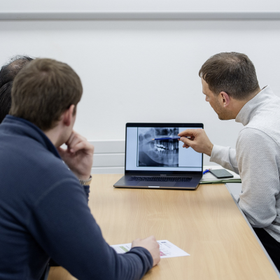 three people looking at a laptop with one describing a dental x-ray to the other two