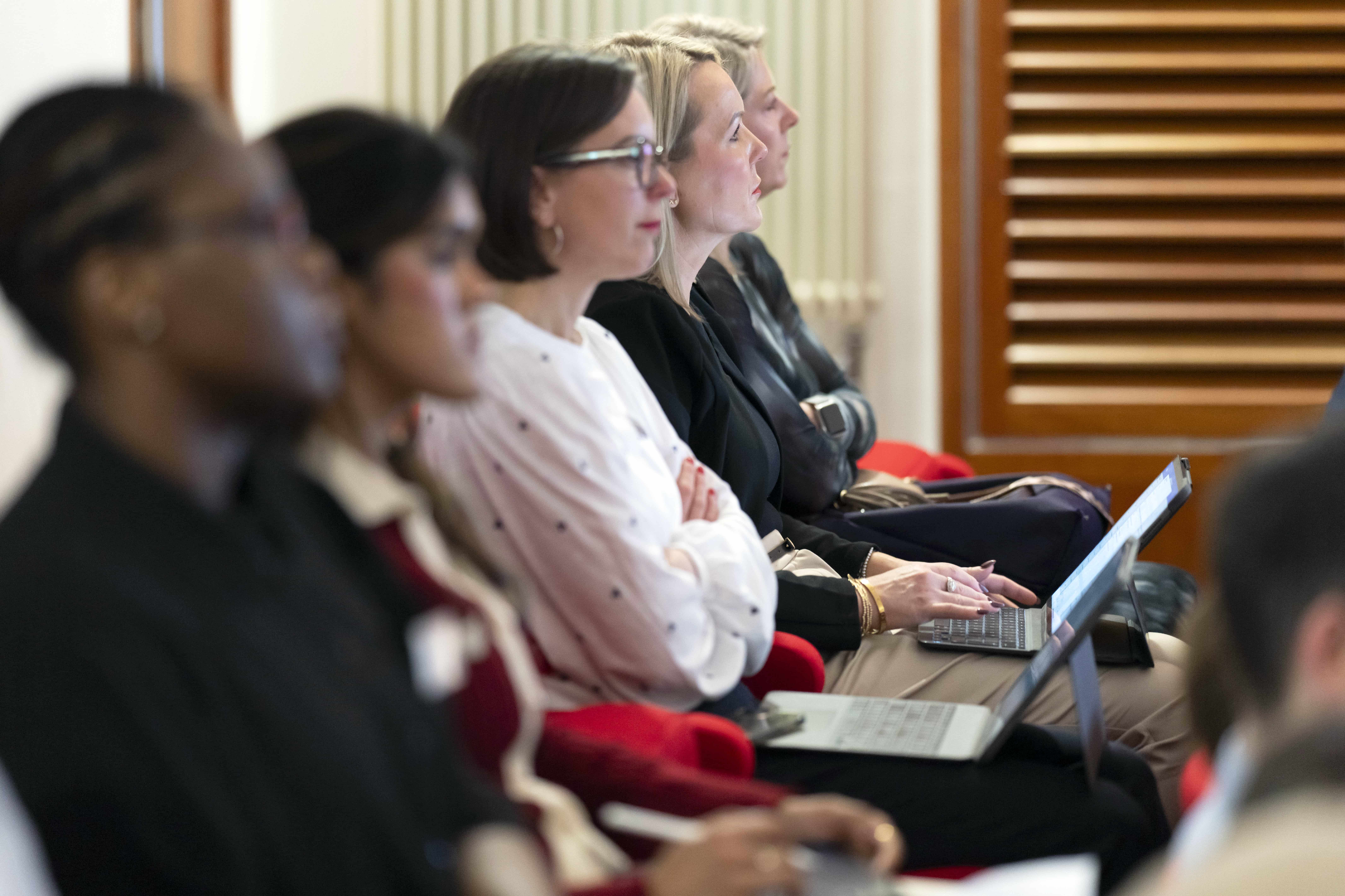 Group of professionals attentively listening and taking notes during a medical education session, some using laptops.